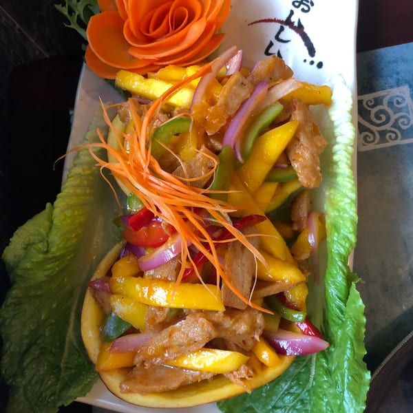 Vegetarian mango salad with bell peppers, red onions, and carrot garnish, served in a mango half.