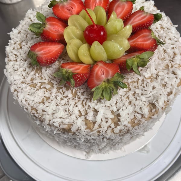 A vegetarian cake covered in shredded coconut, topped with strawberries, green grapes, and a cherry.