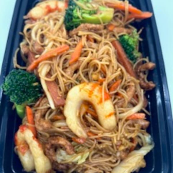 Vegetarian chow mein with noodles, broccoli, carrots, and plant-based shrimp in a black container.