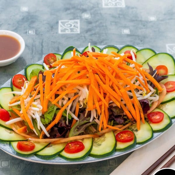 A vibrant vegetarian salad with shredded carrots, bean sprouts, mixed greens, cucumber slices, and cherry tomatoes.