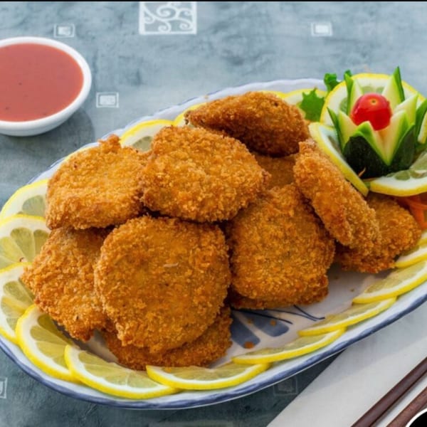 Crispy vegetarian nuggets with lemon slices and a decorative cucumber garnish, served with dipping sauce.