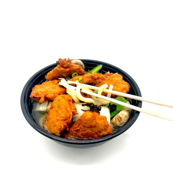 Vegetarian noodle soup with fried tofu, mushrooms, and greens in a black bowl with chopsticks.